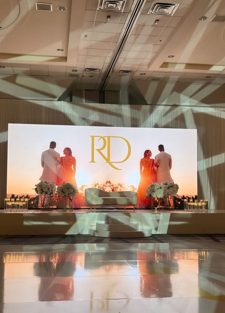 Reception stage with a large screen, florals and a monogrammed dance floor