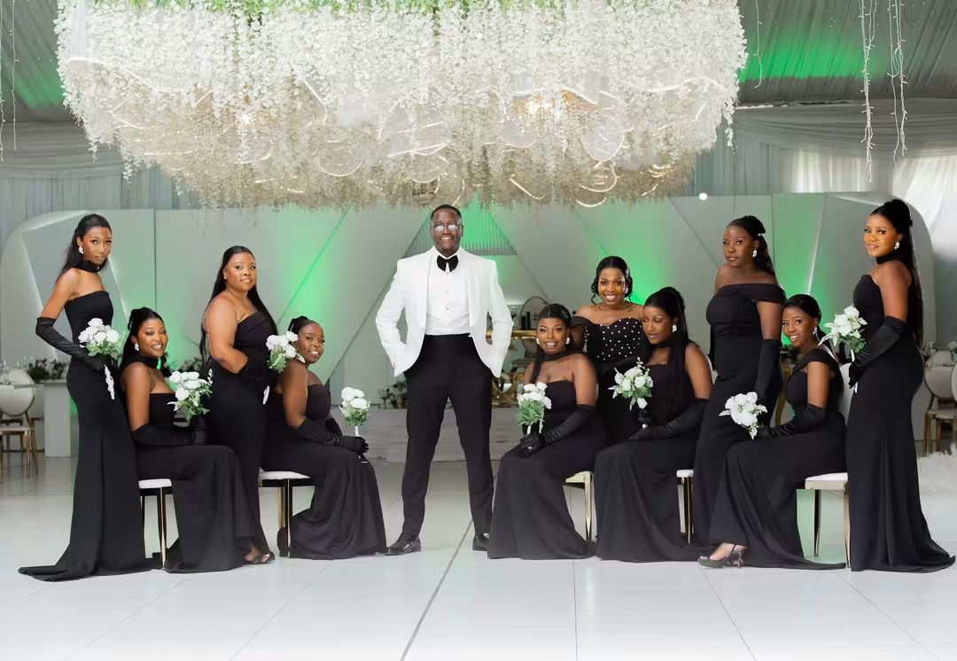 Groom with the bridesmaids in black gowns beneath the suspended floral installation