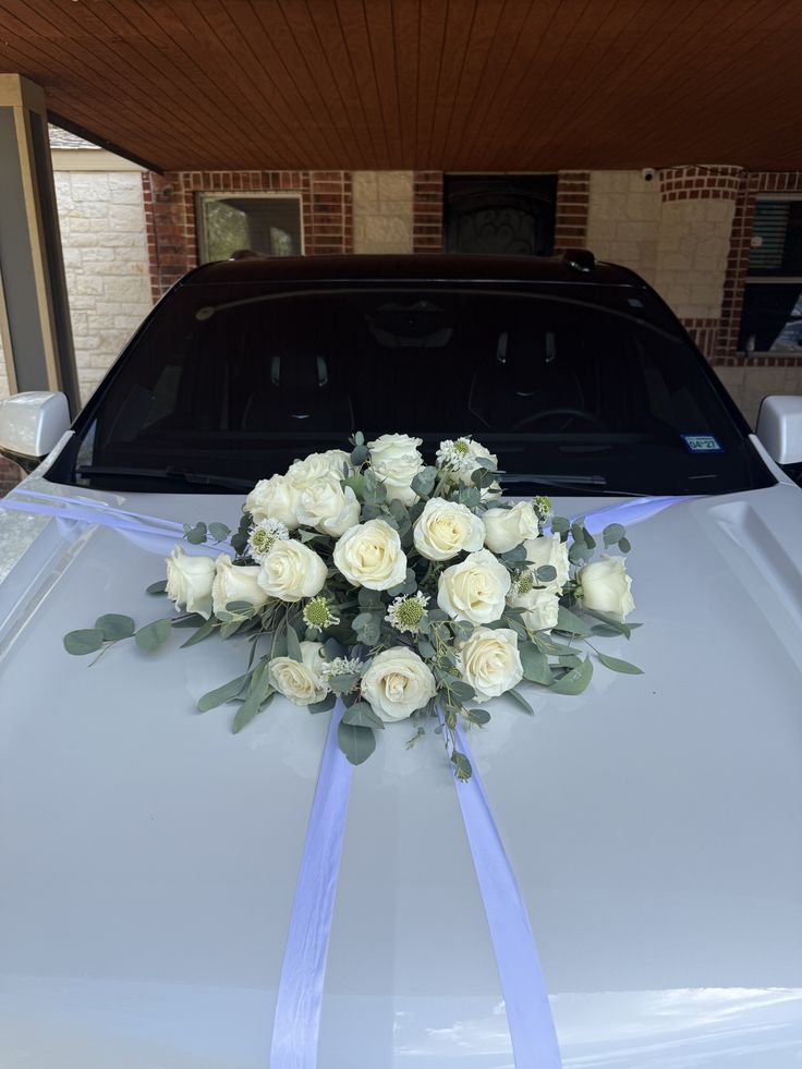 White wedding car decorated with white roses, greenery and ribbon across the bonnet
