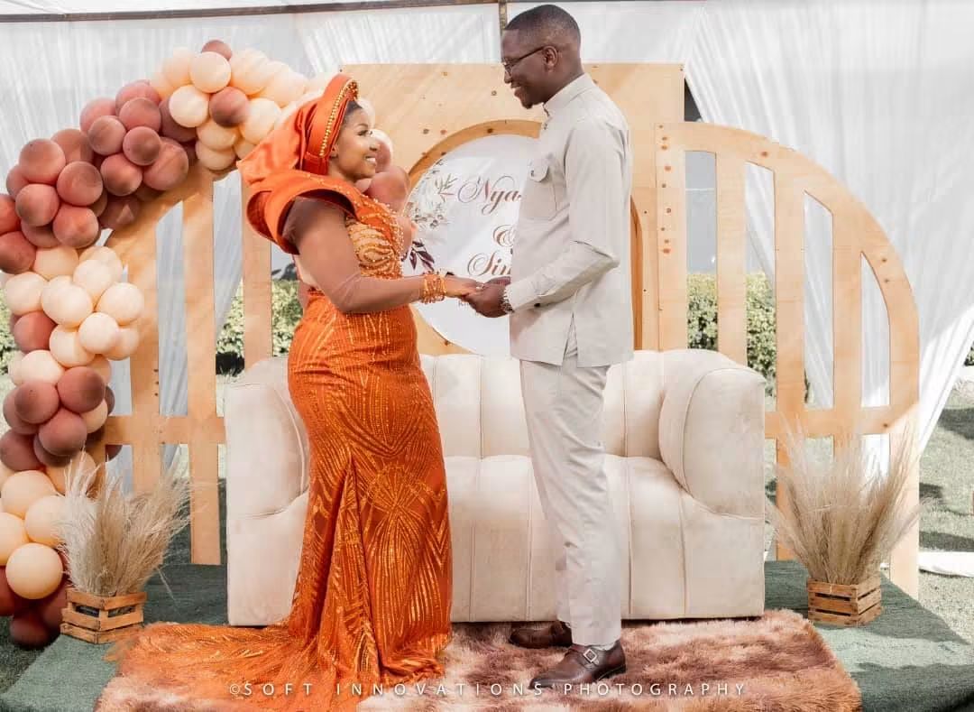 Nyasha and Simba holding hands in front of their personalised roora backdrop